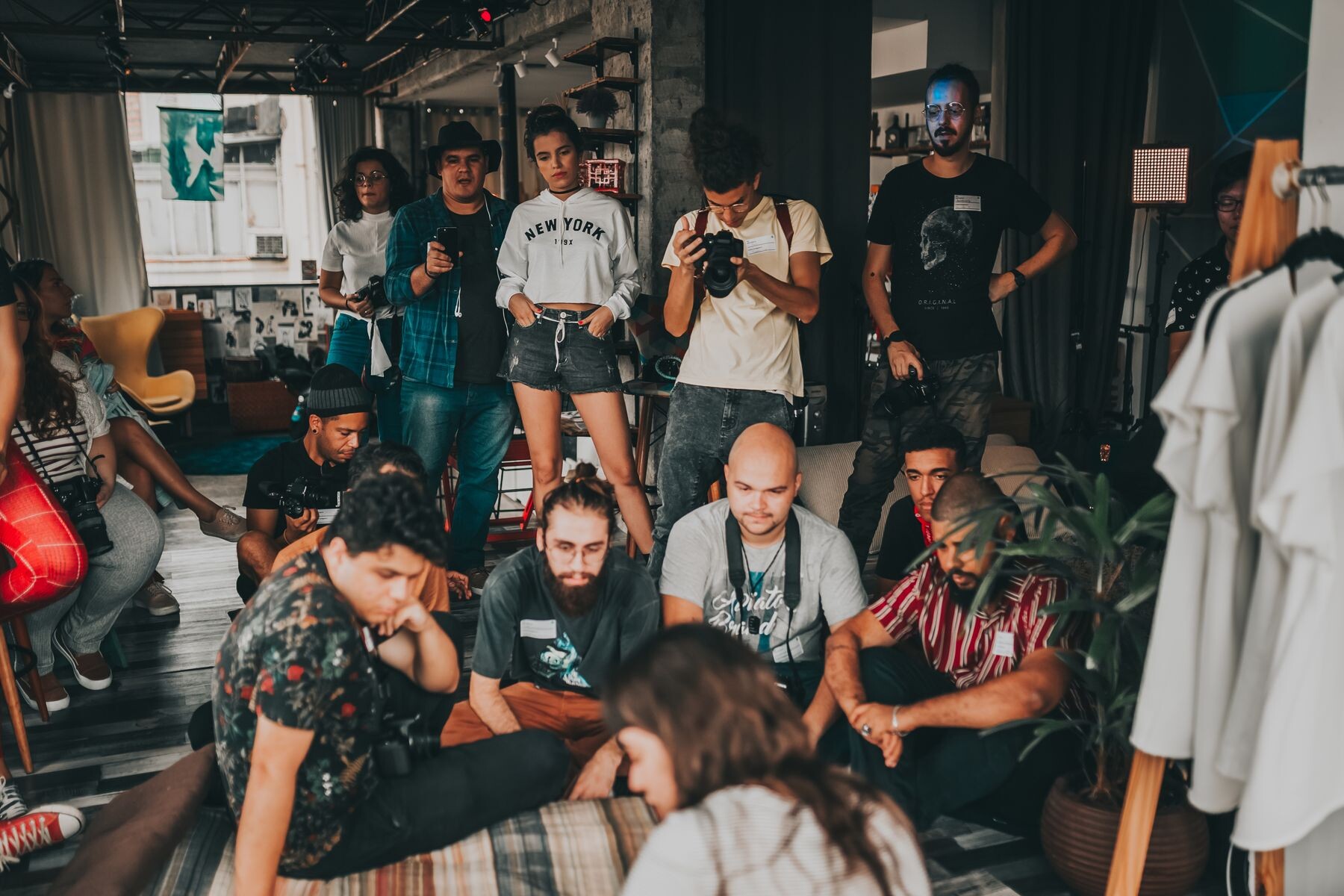 People sitting and standing in a room, several holding cameras.